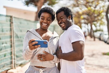 Poster - African american man and woman couple watching video on smartphone at street