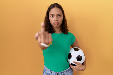 Wall Mural - Young hispanic woman holding ball showing middle finger, impolite and rude fuck off expression