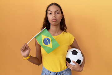 Wall Mural - Young hispanic woman holding brazil flag and football ball skeptic and nervous, frowning upset because of problem. negative person.