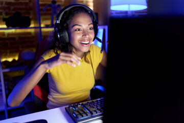 Wall Mural - Young african american woman streamer playing video game using computer at gaming room