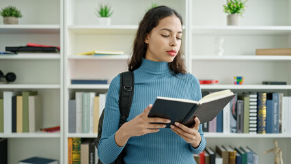 Poster - Young beautiful hispanic woman student standing reading book at university classroom