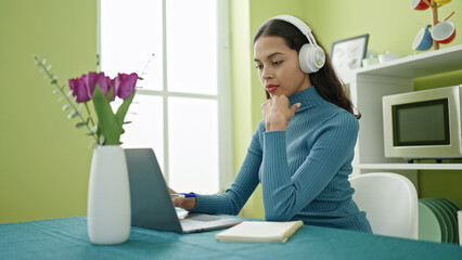 Poster - Young beautiful hispanic woman using laptop and headphones sitting on table at home