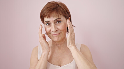 Canvas Print - Mature hispanic woman looking serious touching face with hand over isolated pink background