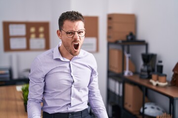 Sticker - Young hispanic man at the office angry and mad screaming frustrated and furious, shouting with anger. rage and aggressive concept.