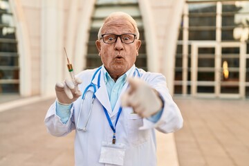 Canvas Print - Senior doctor with grey hair holding syringe pointing with finger to the camera and to you, confident gesture looking serious