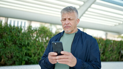 Poster - Middle age grey-haired man using smartphone with serious expression at park