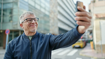 Wall Mural - Middle age grey-haired man smiling confident making selfie by the smartphone at street