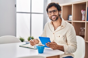 Wall Mural - Young hispanic man writing on notebook using touchpad at home