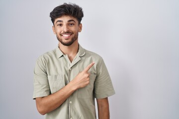 Poster - Arab man with beard standing over white background cheerful with a smile on face pointing with hand and finger up to the side with happy and natural expression