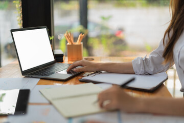 An Asian businesswoman working at her desk in the office, using laptop computer, searching information on the website. laptop white screen mockup.