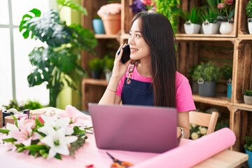 Poster - Young chinese woman florist talking on smartphone using laptop at flower shop