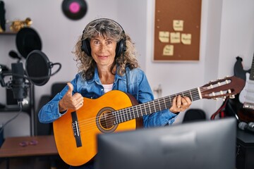 Canvas Print - Middle age woman playing classic guitar at music studio smiling happy and positive, thumb up doing excellent and approval sign