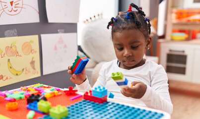 Wall Mural - African american girl playing with construction blocks sitting on table at kindergarten