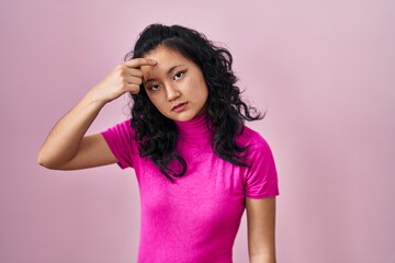 Poster - Young asian woman standing over pink background pointing unhappy to pimple on forehead, ugly infection of blackhead. acne and skin problem