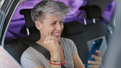 Young woman passenger sitting on car using smartphone celebrating at street