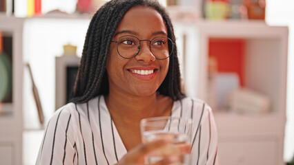 Wall Mural - African american woman drinking water sitting on table speaking at dinning room