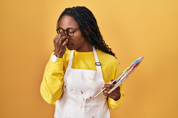 Wall Mural - African woman holding painter palette tired rubbing nose and eyes feeling fatigue and headache. stress and frustration concept.