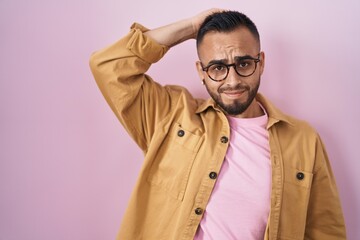 Poster - Young hispanic man standing over pink background confuse and wonder about question. uncertain with doubt, thinking with hand on head. pensive concept.