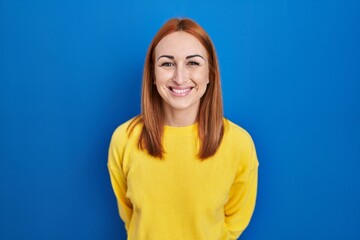 Wall Mural - Young woman standing over blue background with a happy and cool smile on face. lucky person.