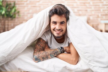 Sticker - Young hispanic man lying on bed covering with bedsheet at bedroom