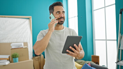 Sticker - Young hispanic man talking on smartphone using touchpad at new home