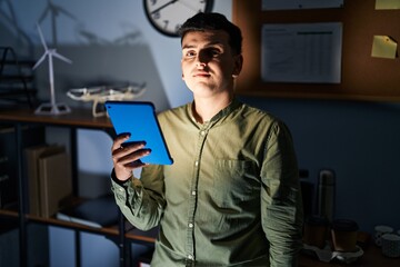 Non binary person using touchpad device at night relaxed with serious expression on face. simple and natural looking at the camera.