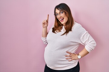 Canvas Print - Pregnant woman standing over pink background pointing finger up with successful idea. exited and happy. number one.