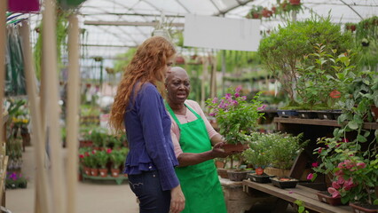 Wall Mural - Senior Lady Helping Young Female Client at Local Gardening Shop. An African American elder woman advising customer on plant purchase in a small business Flower Store