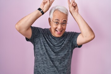 Canvas Print - Middle age man with grey hair standing over pink background posing funny and crazy with fingers on head as bunny ears, smiling cheerful