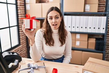 Sticker - Young hispanic doctor woman working at small business ecommerce holding present scared and amazed with open mouth for surprise, disbelief face