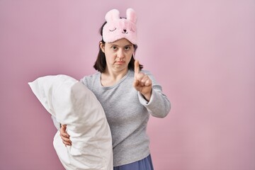 Wall Mural - Woman with down syndrome wearing sleeping mask hugging pillow pointing with finger up and angry expression, showing no gesture