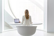 © Elena - Woman sitting on big chair working on laptop in white office, rear view. Generative AI