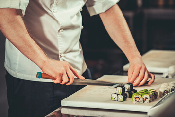 Wall Mural - Chef in hotel or restaurant kitchen cooking, only hands. He is working on maki rolls. Preparing sushi set