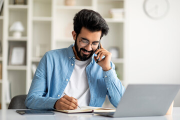 Wall Mural - Young Indian Male Talking On Cellphone And Taking Notes To Notepad