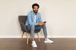 © Prostock-studio - Cheerful Young Indian Man With Smartphone In Hands Relaxing In Armchair Indoors