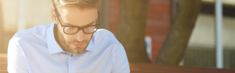 Business message. Focused businessman using smartphone and drinking coffee while sitting on the bench outdoors