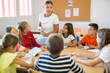© JackF - Teacher explaining subject to children during lesson in school. Kids sitting around table and listening carefully to teacher.