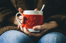 Red Knitted Woolen Cup With Heart Pattern In Female Hands. Hands Holding A Cozy Mug In Red Knitted Mitten With Hot Cocoa, Tea Or Coffee. Valentines Day Concept