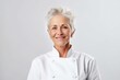 Portrait of smiling senior woman in chef uniform standing against white background