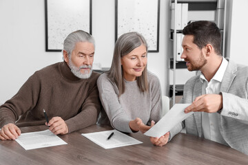 Elderly couple consulting insurance agent about pension plan at wooden table indoors