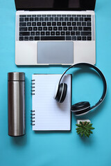 Top view of blue background with laptop, headphone, steel reusable thermo bottle, succulent and notebook