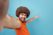 © khosrork - Portrait of king pleased man with Afro hairstyle broadcasting livestream, talking to followers, inviting friends, showing welcome gesture, POV. Indoor studio shot isolated on blue background.