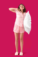 Poster - Young brunette woman in pajamas with pillow on pink background