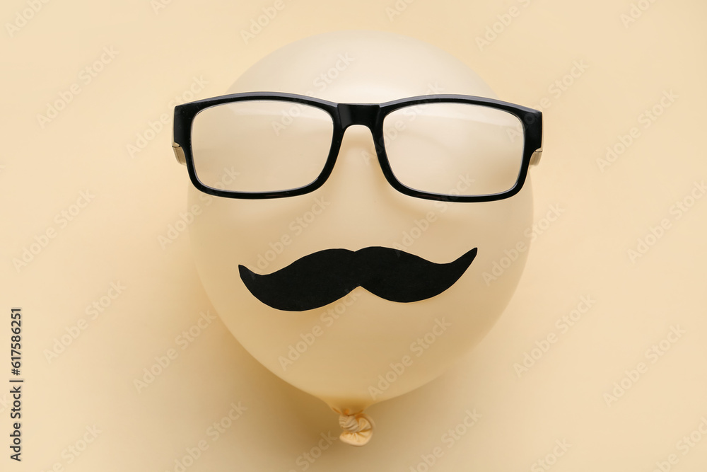 Balloon with paper mustache and eyeglasses on color background