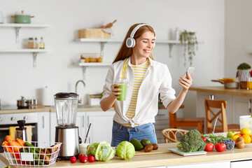 Wall Mural - Young woman in headphones with glass of healthy smoothie and mobile phone at home