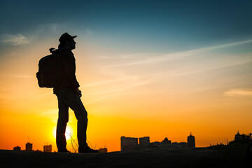 Canvas Print - Traveler silhouette watching amazing sunset. Young casual man with backpack and cowboy hat standing alone on hill above evening cityscape. Lifestyle Travel Concept Outdoor Background. Kiev, Ukraine