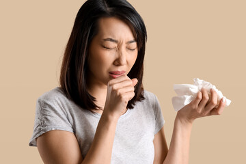 Ill Asian woman with tissues on beige background, closeup