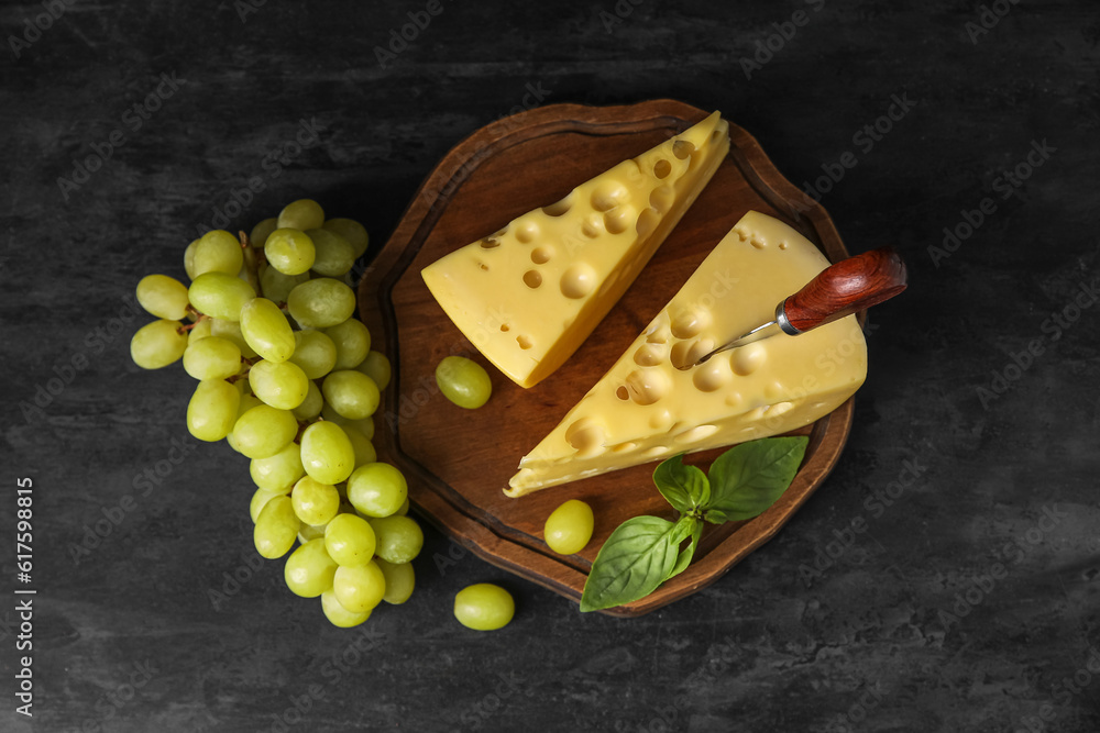Board with tasty Swiss cheese and grapes on black background
