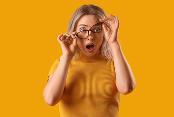 Canvas Print - Surprised young woman in stylish eyeglasses on orange background