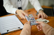 © bongkarn - Close-up image of a professional male banker giving a wad of US dollar bills to a female customer.